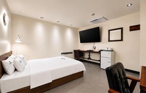 Habitación de hotel con cama, escritorio, silla, televisor y una pequeña cocina.