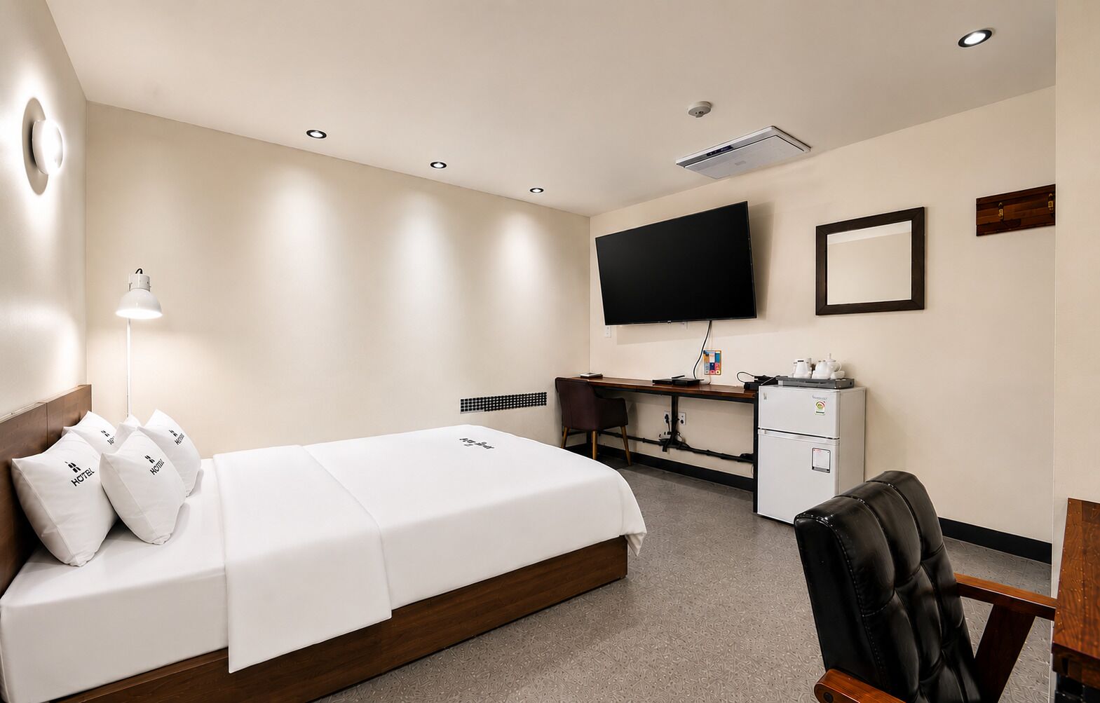 A hotel room with a bed, desk, chair, television, and a minibar.