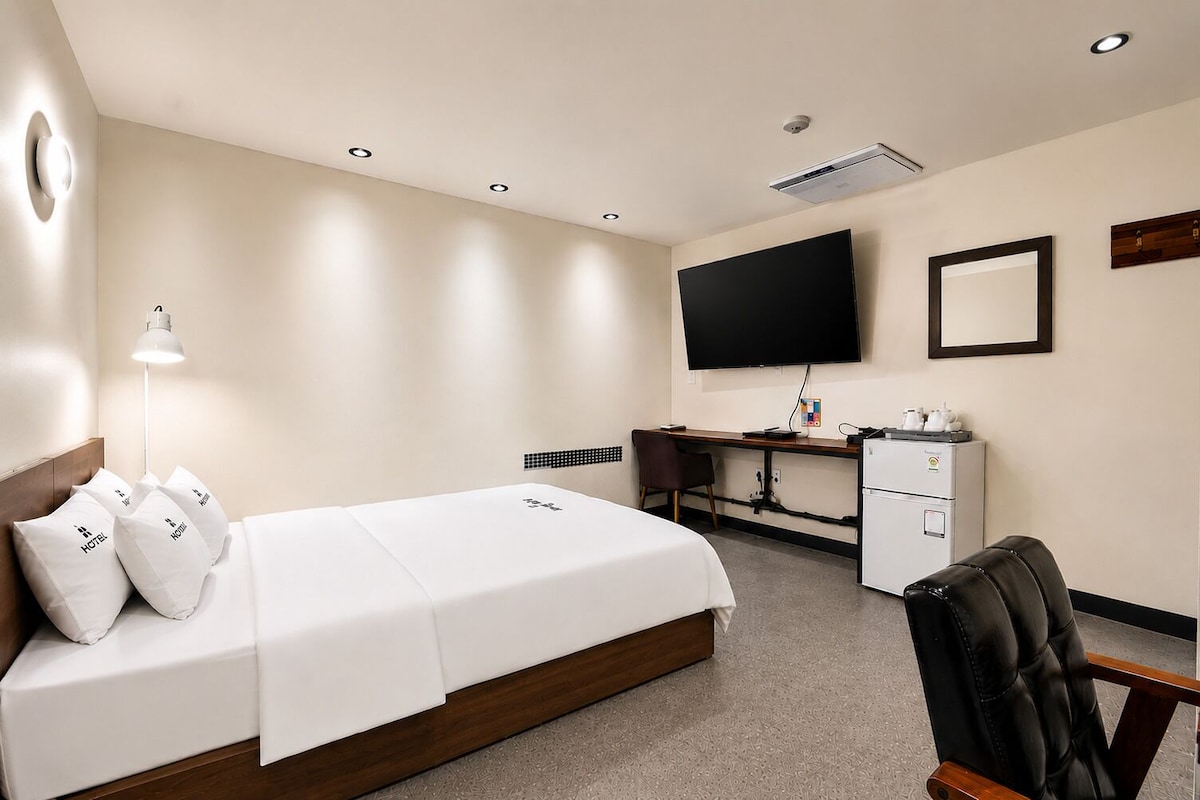 Habitación de hotel con cama, escritorio, silla, televisor y minibar.