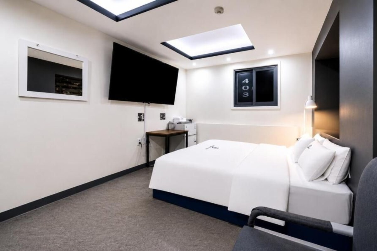 Habitación de hotel con cama, escritorio, silla, televisor y ventana con un cartel con número.