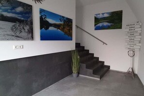 Een trap met een leuning, een bloempot en drie landschapsschilderijen aan de muur.
