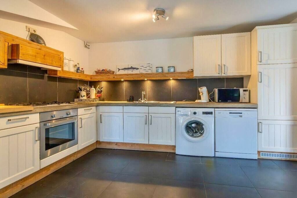 Een moderne keuken met witte kastjes, een inbouwoven, een wasmachine en een magnetron.
