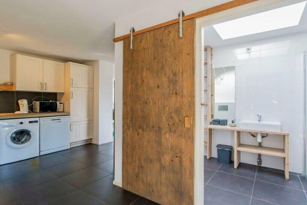 Une cuisine moderne avec des meubles blancs, une porte coulissante en bois et un lave-linge.