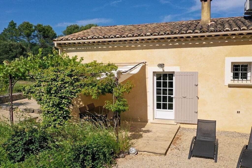 A single-story building with a tiled roof, a door with a window, and a small patio area with a chair.