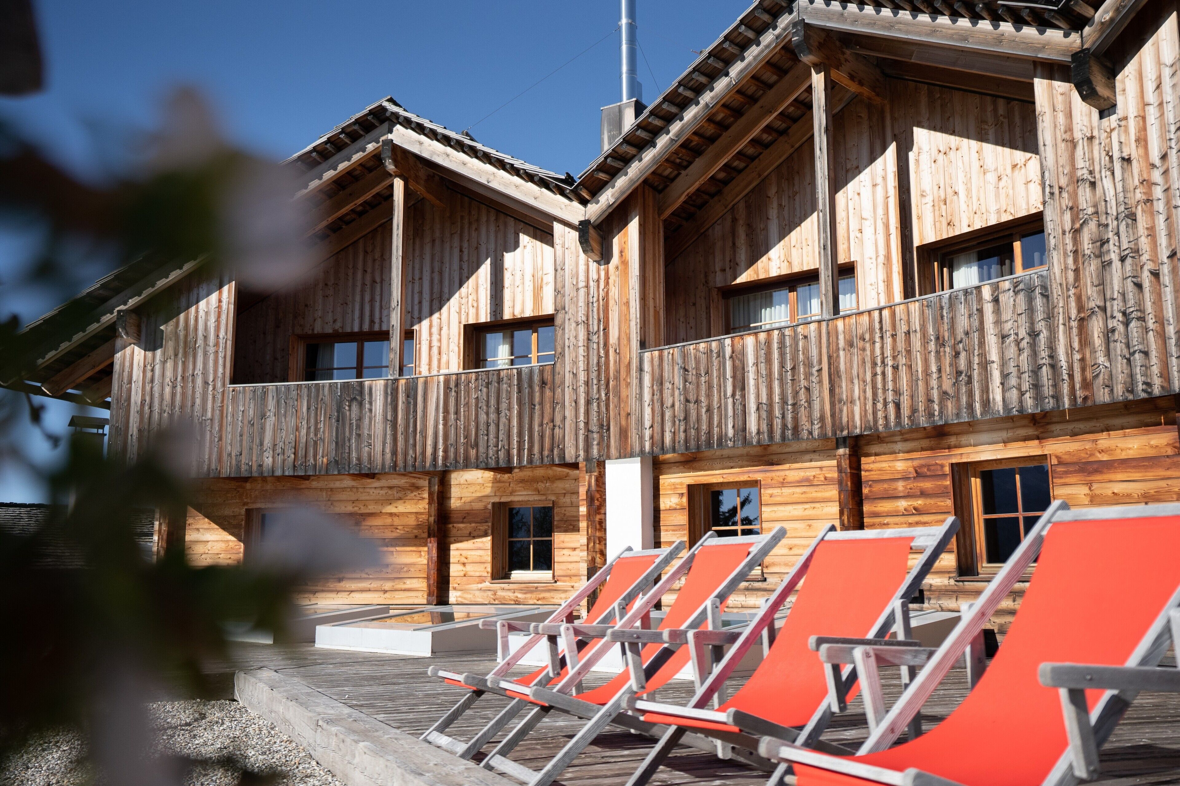 Un bâtiment en bois doté de nombreux balcons et fenêtres, avec des espaces de détente en plein air et des chaises orange.