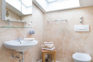 Un baño con tragaluz, un lavamanos, un inodoro y un perchero para toallas.