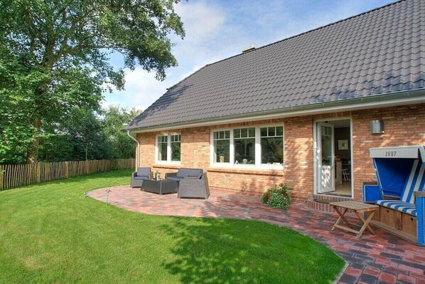 Ein Ziegelhaus mit einem Ziegeldach, einer Terrasse mit Gartenmöbeln und einem umzäunten Garten.