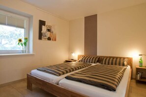 Ein Doppelbett mit gestreifter Bettwäsche, ein Nachttisch mit Lampe und ein Fenster mit Sonnenblumen.