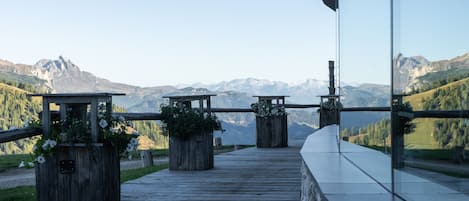 Una terraza de madera con barandilla de vidrio que da a un paisaje montañoso.