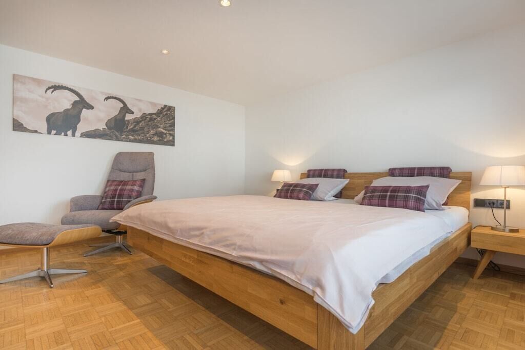 Un dormitorio con cama de madera, una silla, una mesita de noche y una lámpara de pared.