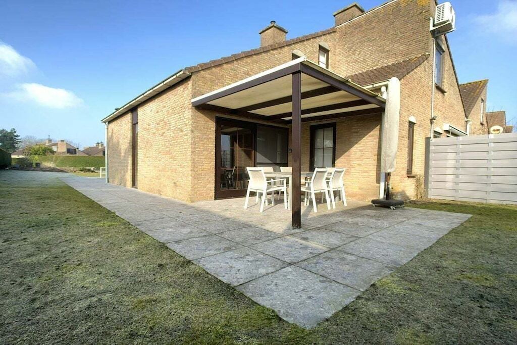 A brick house with a covered patio area, a table, and chairs.