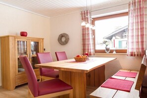 Un comedor con mesa de madera, sillas tapizadas rojas, un armario con puertas de cristal y una ventana con cortinas.