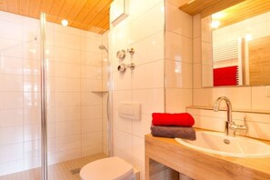 Un baño moderno con cabina de ducha de vidrio, inodoro blanco y tocador de madera con lavabo.
