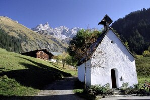 Un edificio blanco con techo pronunciado, un pequeño porche y montañas al fondo.
