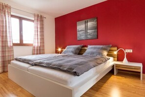 Un dormitorio con una cama, una mesita de noche, una lámpara de pared y un ventanal con cortinas.