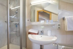 Un baño con ducha de vidrio, lavamanos blanco y espejo sobre él.