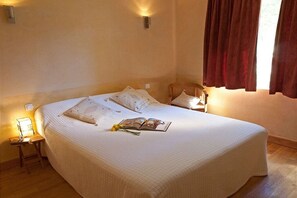 A neatly made bed with pillows and a book, a bedside table with a lamp, and a window with curtains. - Holiday home in Bonnieux with swimming pool (Bonnieux)