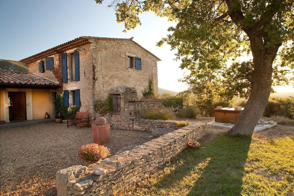 A rustic stone building with a tiled roof, a wooden door, and a bench outside.