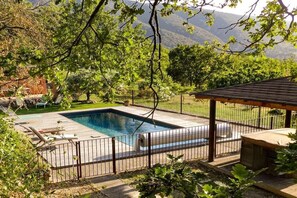 A rectangular swimming pool with a wooden deck and metal railing, surrounded by lush greenery and a mountainous backdrop. - Holiday home in Bonnieux with swimming pool (Bonnieux)
