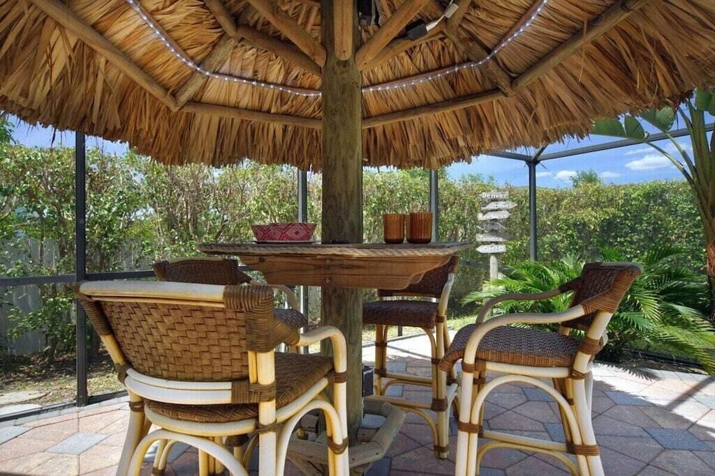 Un área de comedor al aire libre con techo de paja, mobiliario de mimbre y vistas de la vegetación circundante.