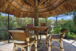 An outdoor dining area with a thatched roof, wicker furniture, and a view of the surrounding greenery. - CCVS - Villa Tropical Dream (Cape Coral SW Florida)