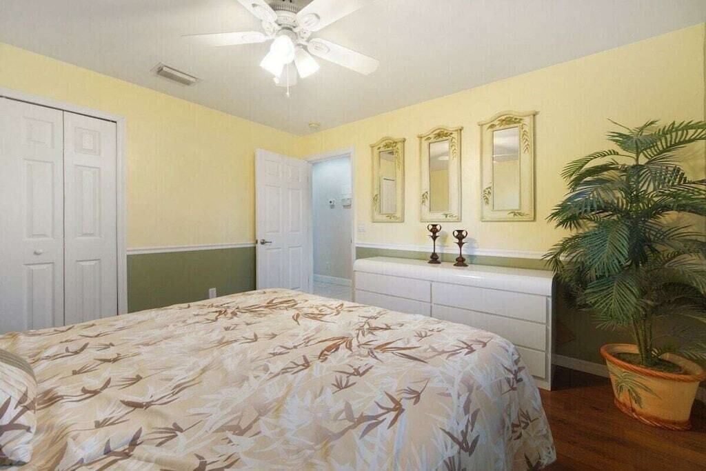 Ein Schlafzimmer mit einem Bett, einem Deckenventilator, einer Topfpflanze und einem Schminktisch mit Spiegeln.