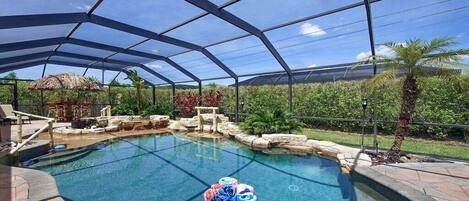 Una piscina techada con borde de piedra, una cesta de mimbre con toallas y una estructura de techo de paja al fondo.