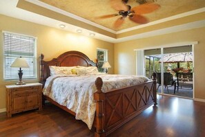 Ein Schlafzimmer mit einem hölzernen Bett, einem Deckenventilator und Blick auf eine Terrasse.