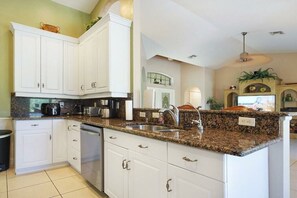 A kitchen with white cabinets, granite countertops, and a built-in dishwasher. - CCVS - Villa Tropical Dream (Cape Coral SW Florida)