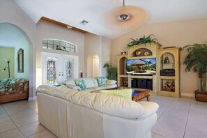 A spacious living room with a large beige sofa, a flat-screen TV, and a fireplace. - CCVS - Villa Tropical Dream (Cape Coral SW Florida)