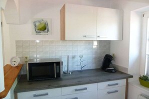 A kitchen with white cabinets, a microwave, a coffee maker, and a clock on the counter. - Holiday apartment in Wiek with barbecue (Wiek)
