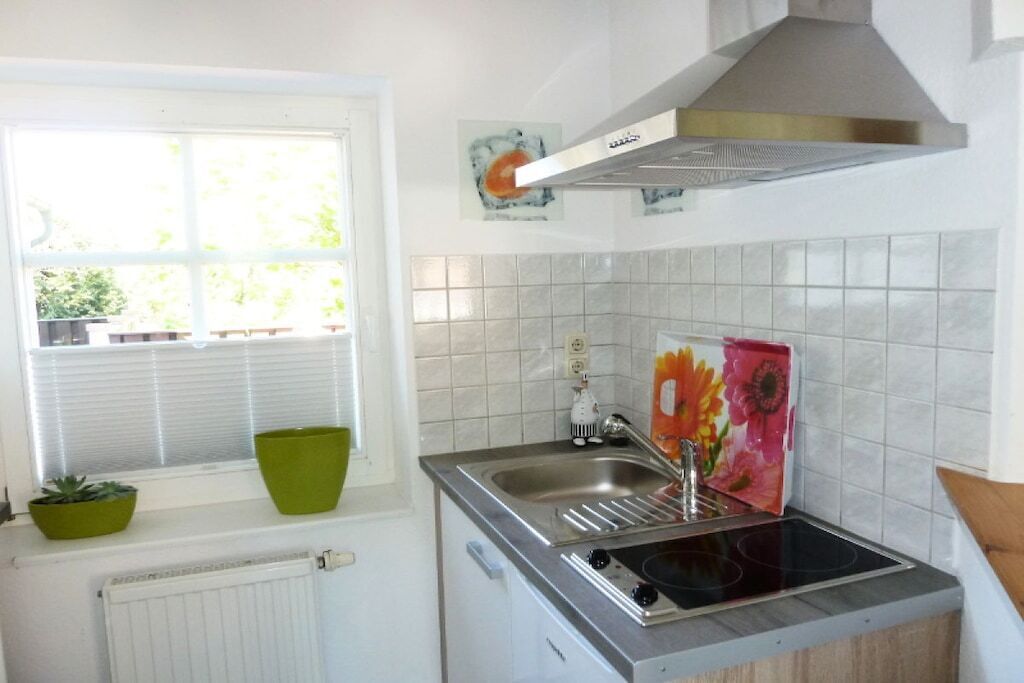 A compact kitchen with a window, a radiator, a sink, and a stove.