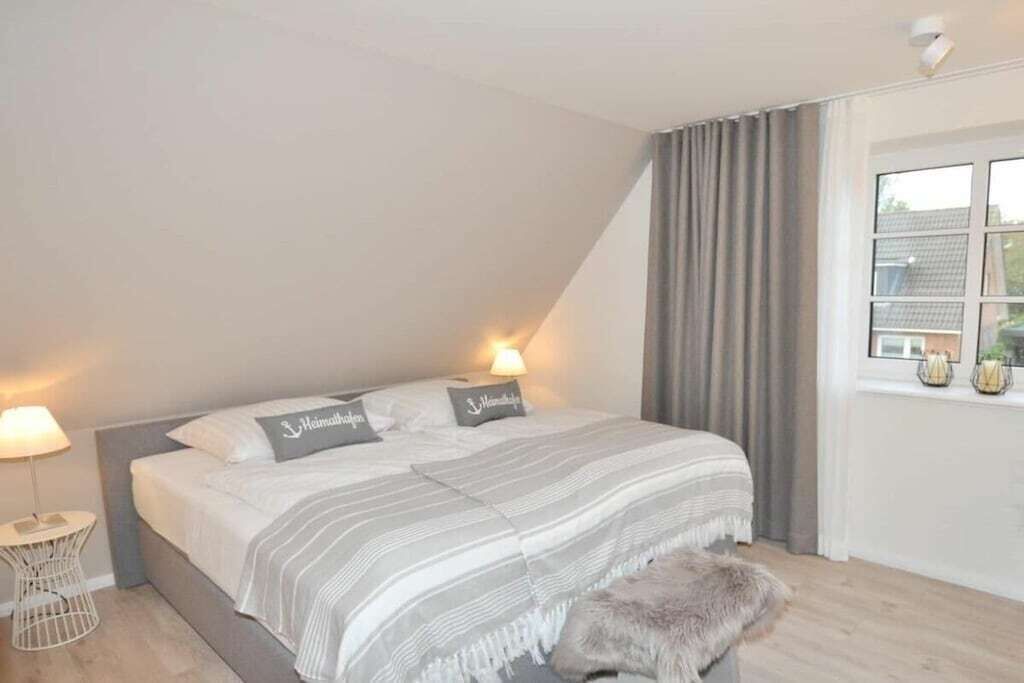 A bedroom with a bed, bedside lamps, a window with curtains, and a small table with a lamp.