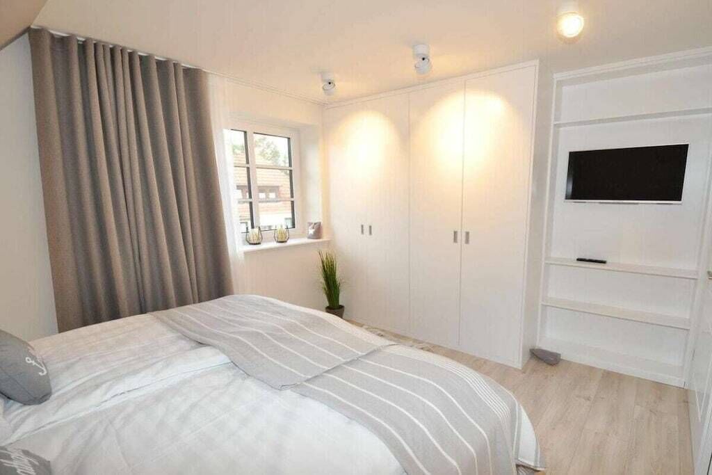 A bedroom with a bed, a TV mounted on the wall, and a window with curtains.