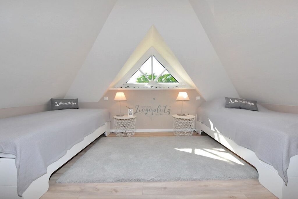 Una stanza con soffitto spiovente, due letti con biancheria bianca, due comodini con lampade e una finestra all'apice del soffitto.