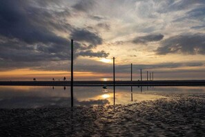 Ruhige Strandansicht bei Sonnenuntergang, ruhiges Wasser und wenige Spaziergänger.