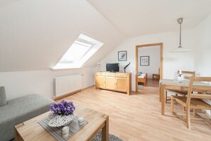 Ein modernes Loft-Apartment mit schrägverdeckter Decke, einem Essbereich mit Holzmöbeln, einem grauen Sofa und einem kleinen Tisch mit einer Blumenvase.