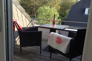 Un balcón con una mesa, sillas, una botella de vino y una copa.