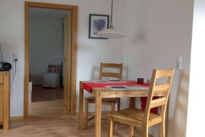 Un comedor con una mesa y sillas de madera, una lámpara colgante y una puerta que da a otra habitación.