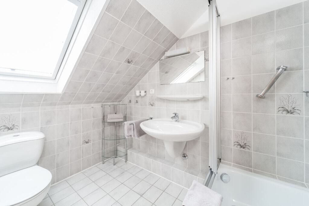 A modern bathroom with a skylight, a white sink, a toilet, and a shower area.