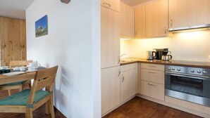 Cocina compacta con armarios de madera, horno de acero inoxidable y comedor con mesa y sillas de madera.