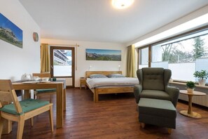 Ein Zimmer mit einem Bett, einem Sessel, einem Tisch und einem Fenster.