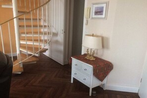 A room with a wooden staircase, a white bedside table with drawers, a lamp, and a framed picture on the wall. - Villa Bernstein Apt. 32 (Binz)