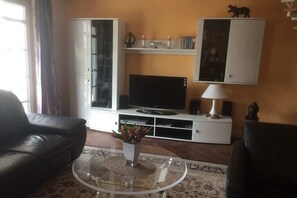 A living room with a sofa, a glass coffee table, a flat-screen TV, a cabinet with decorative items, and a lamp. - Villa Bernstein Apt. 32 (Binz)