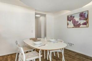 Ein Essbereich mit einem runden Tisch, weißen Stühlen und einem Gemälde an der Wand.