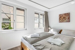 Ein Schlafzimmer mit zwei Betten, einem Fenster mit Vorhängen und einem Bild an der Wand.
