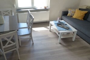 Ein Zimmer mit einem weißen Schreibtisch, einem grauen Sofa und einem kleinen weißen Couchtisch.
