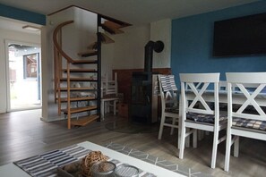 Ein modernes Wohnzimmer mit Wendeltreppe, Kamin und Essbereich mit weißen Stühlen.