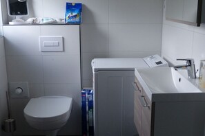 Ett litet badrum med toalett, tvättmaskin och handfat.