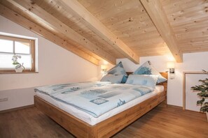 Une chambre avec un plafond en bois, un lit avec une literie bleue et une fenêtre agrémentée d’une plante.
